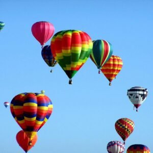 Colorful hot air balloons floating in a clear blue sky, showcasing a vibrant festival scene.