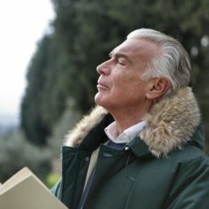 Senior man with white hair, eyes closed enjoying fresh air in Tuscany's natural setting.