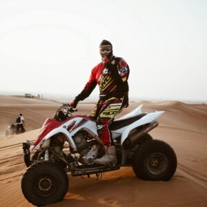 A male rider on an ATV navigating the sand dunes during the day, wearing protective gear and a helmet.