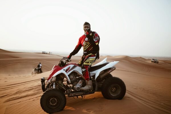 A male rider on an ATV navigating the sand dunes during the day, wearing protective gear and a helmet.